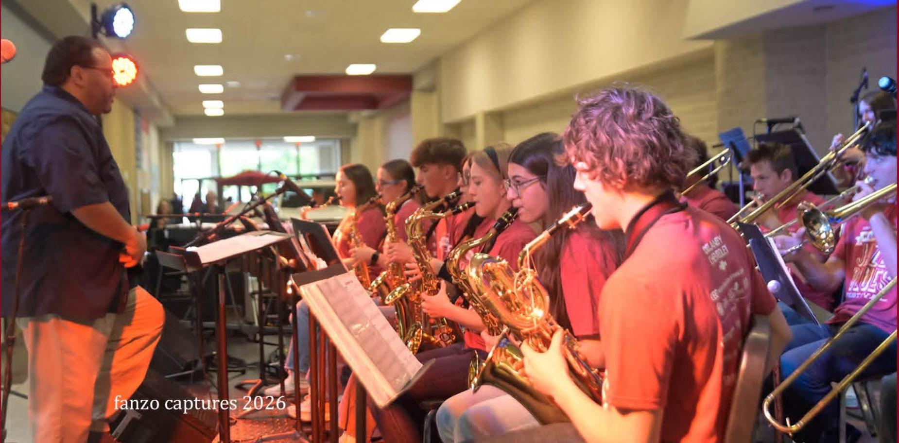 Musicians in red shirts perform in a school auditorium.