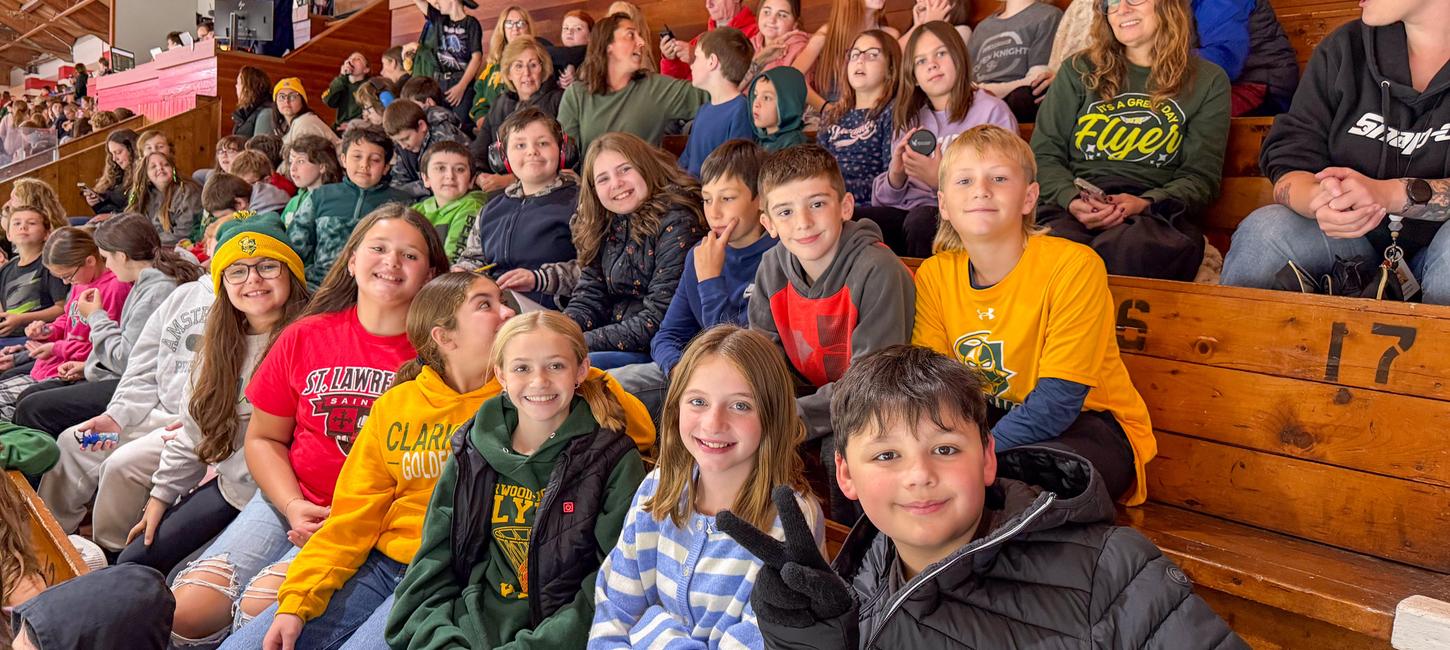 A group of students smile while sitting in the stands of an athletic event