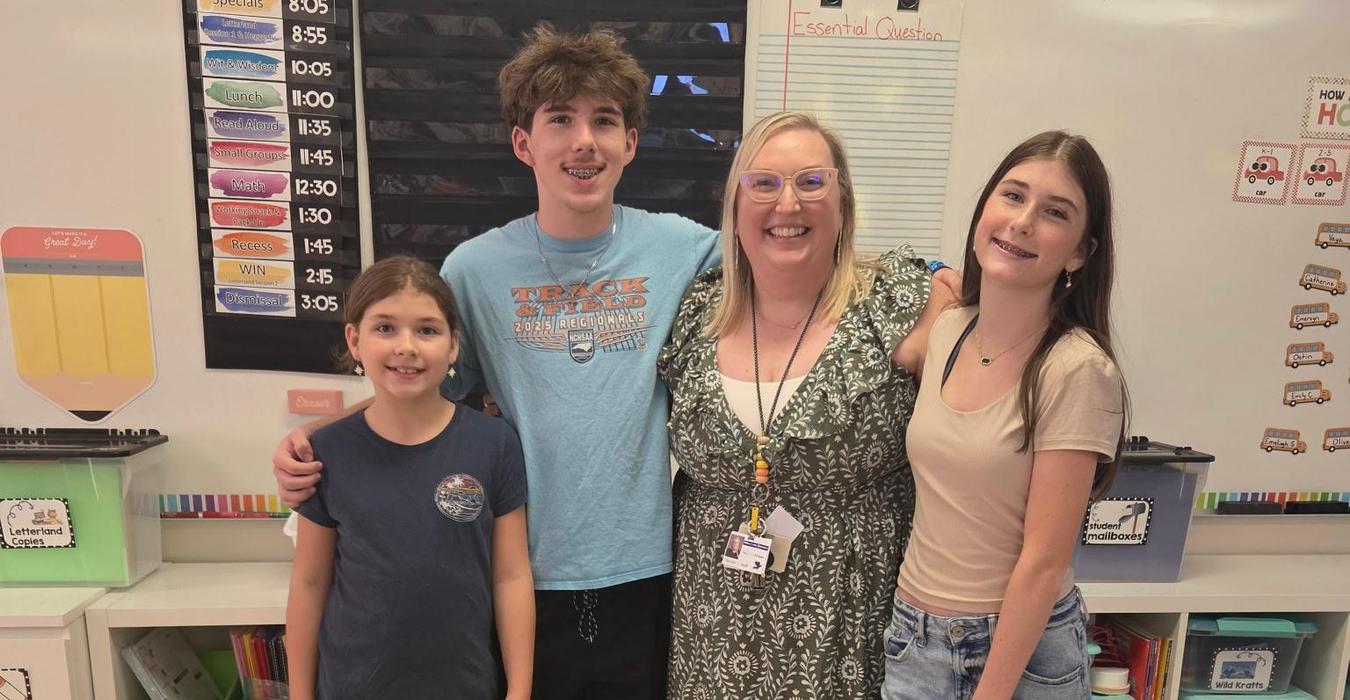 A group standing together in a classroom, including a teacher and students.
