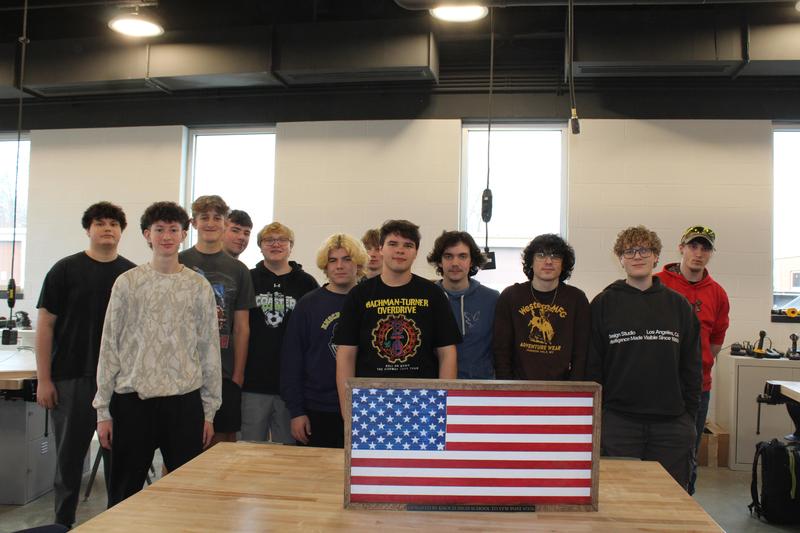 tech ed students standing around wooden flag they created