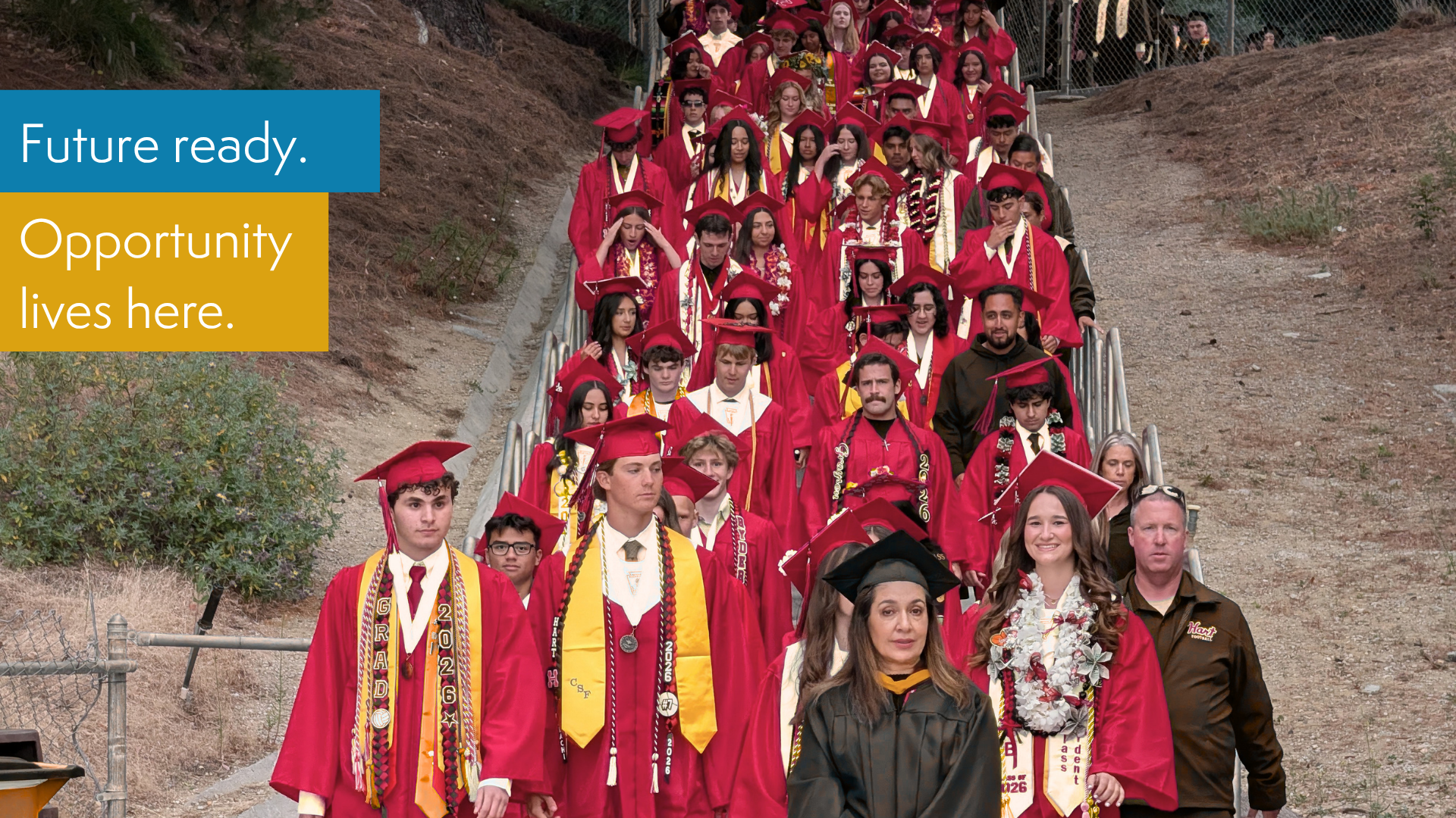 A group of graduates in red gowns proceeding down steps with motivational text.