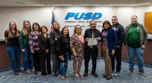 Placido Flores holds his School Employee of the Year certificate surrounded by colleagues at the PUSD Board meeting.