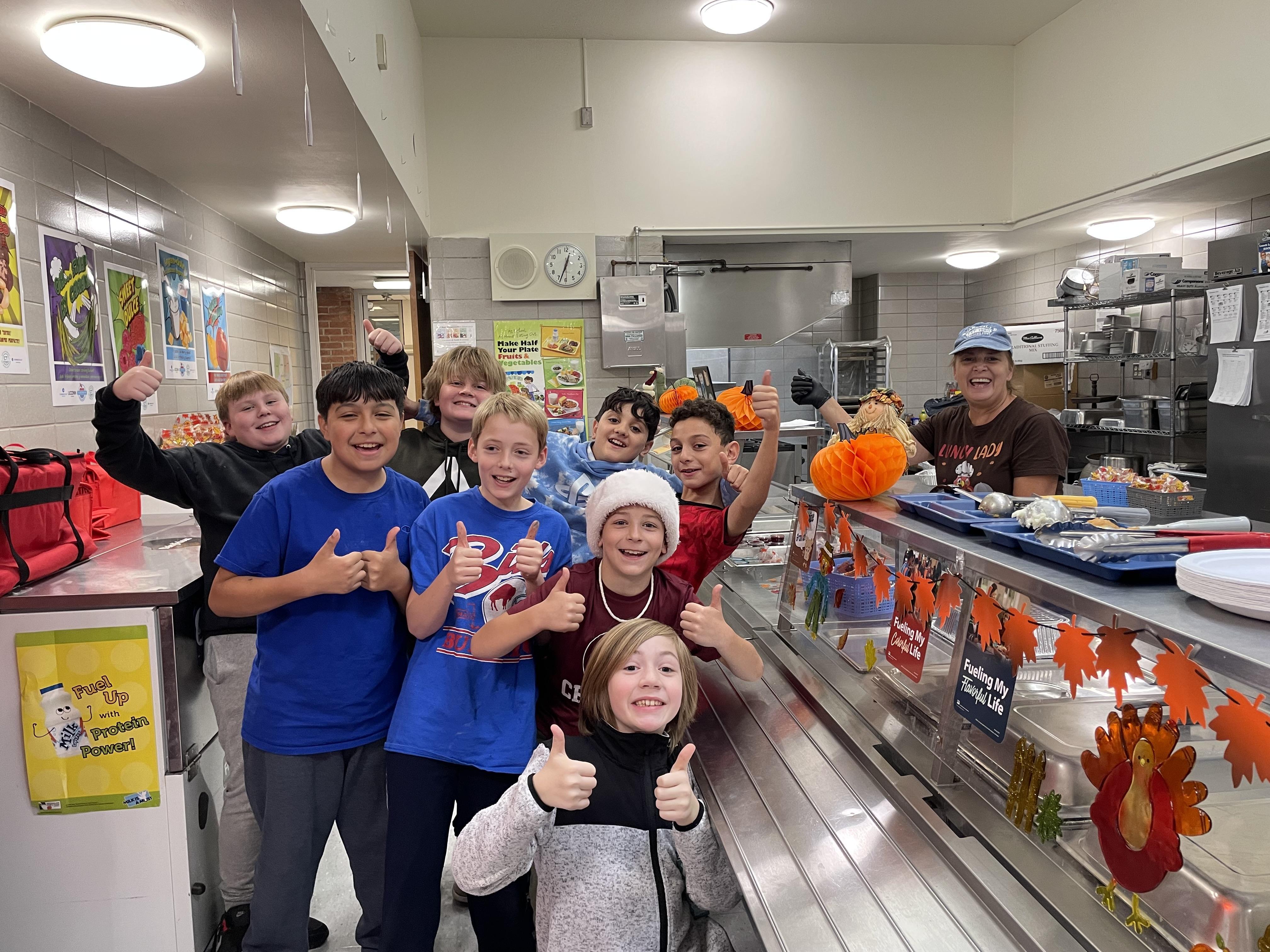 a group of students in the cafeteria smiling at the camera with a cafeteria working smiling in the background