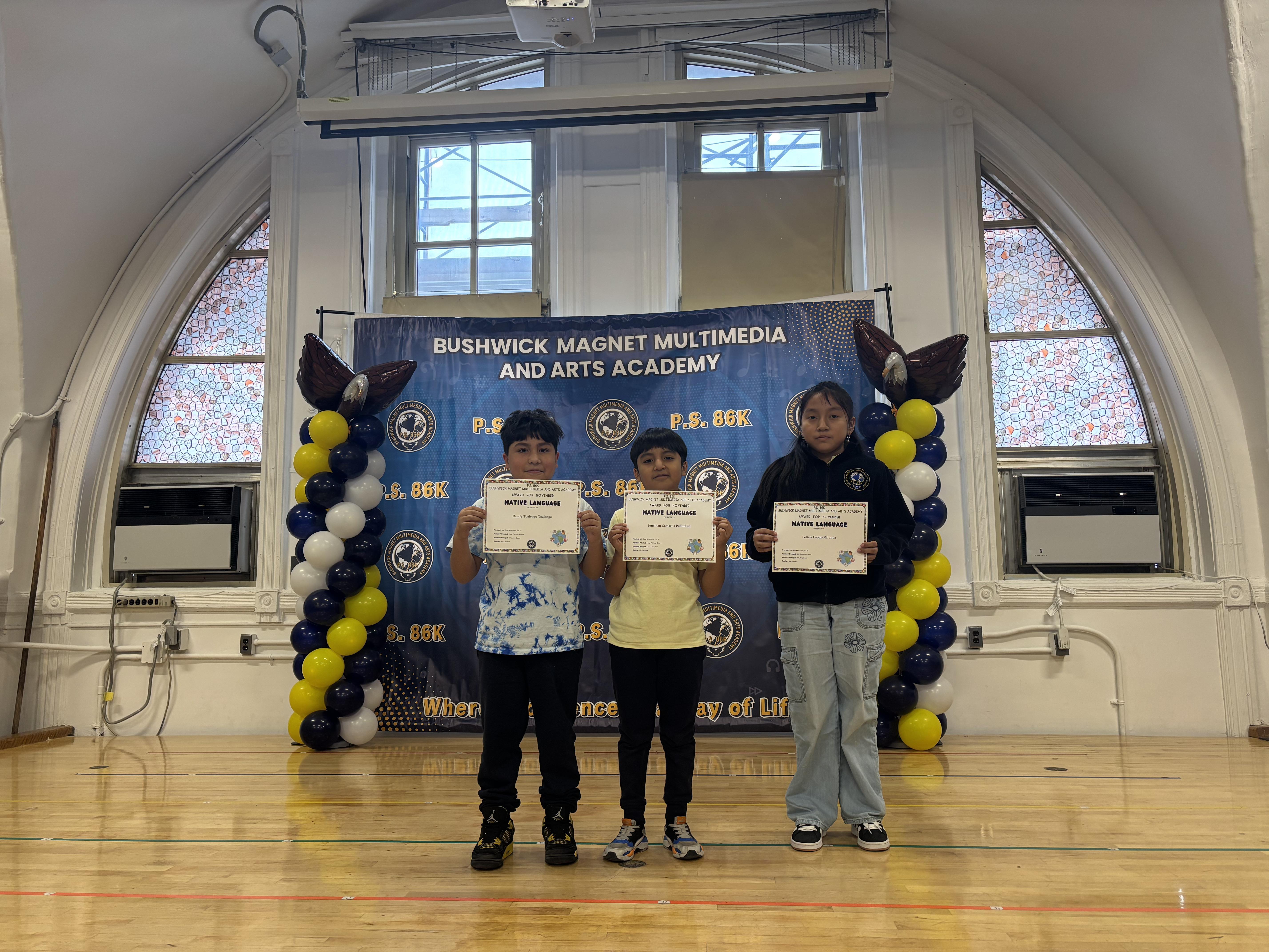 three students on stage holding awards