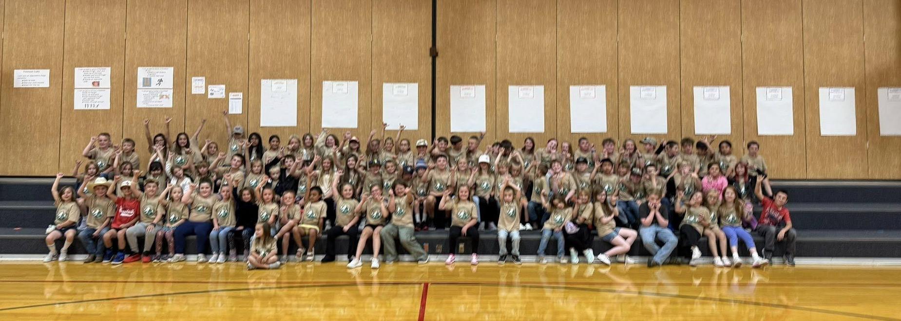 A large group of children in matching shirts smiling and posing on bleachers.