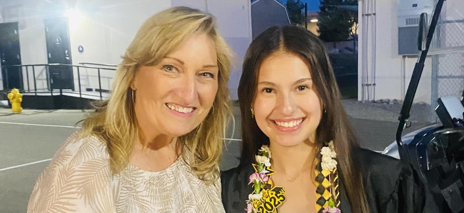 Two women smiling together, one holding a diploma, celebrating graduation.