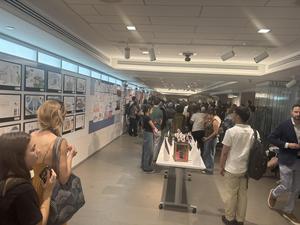 A crowded hallway with people, attending an exhibition filled with artwork displays.