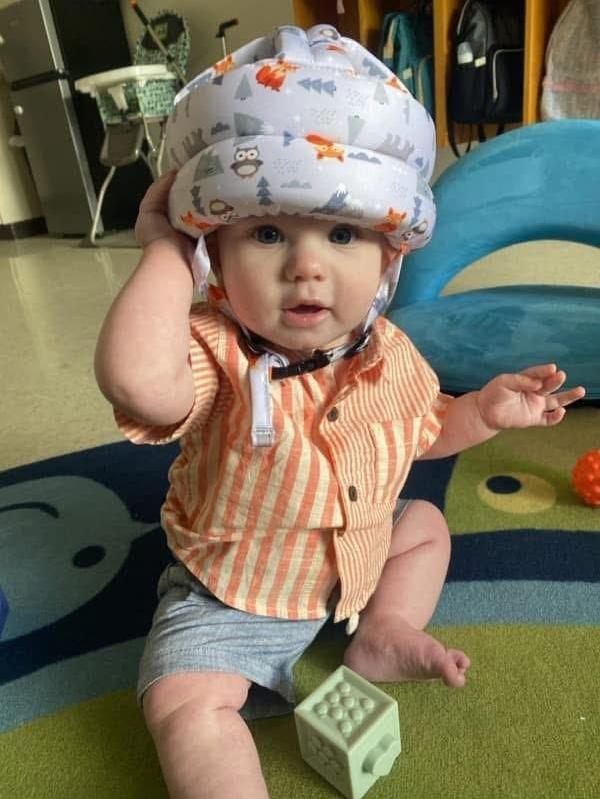 A baby wearing a protective helmet, sitting on a colorful play mat.