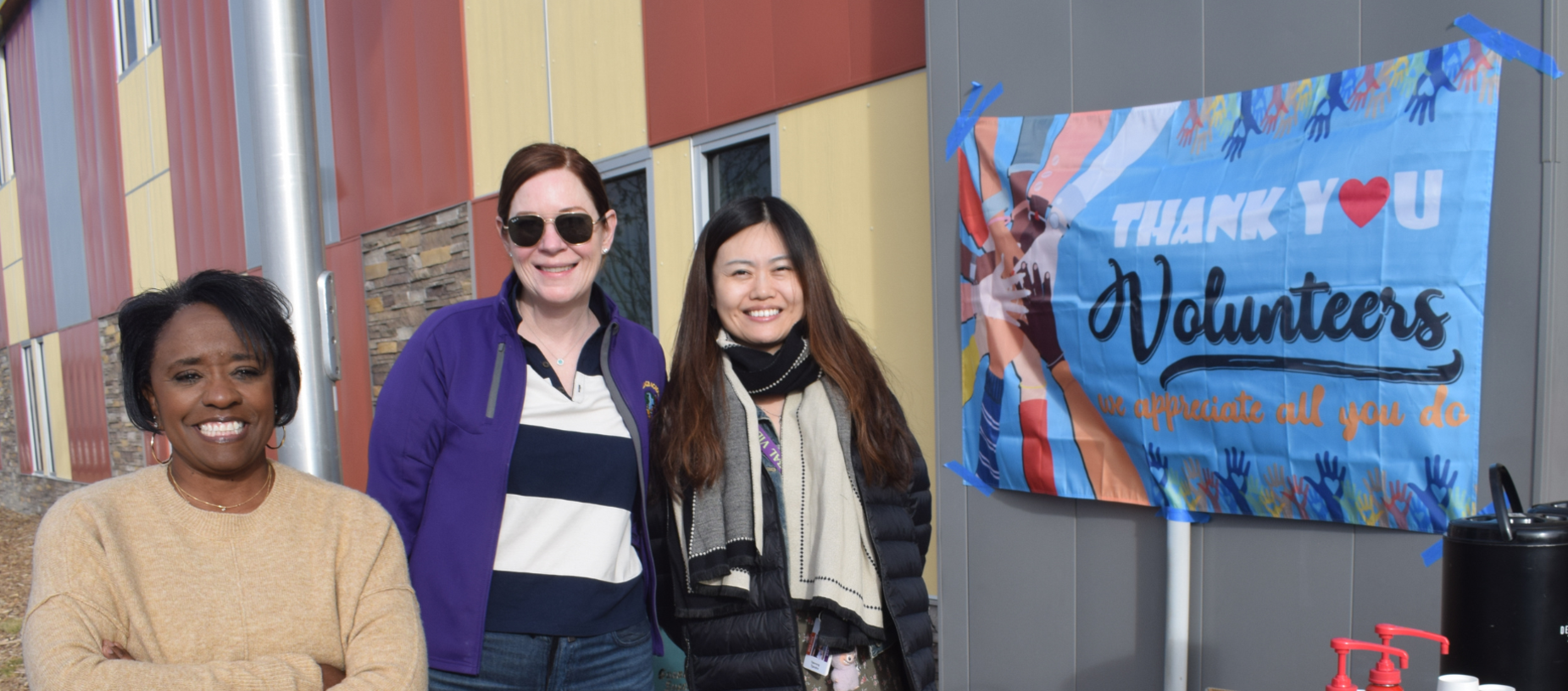 Three volunteers smiling in front of a thank you banner.