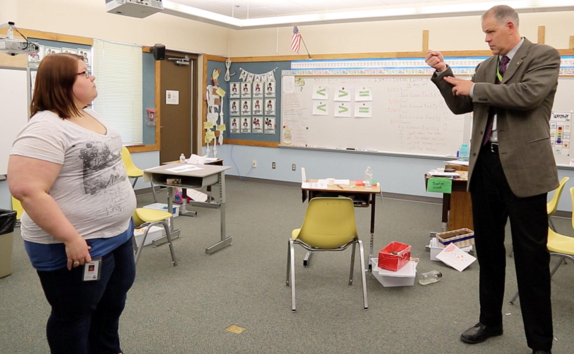 a man and a teacher speak and sign, inside of a classroom
