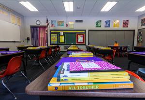 Image shows an empty classroom with a stack of notebooks in the foreground