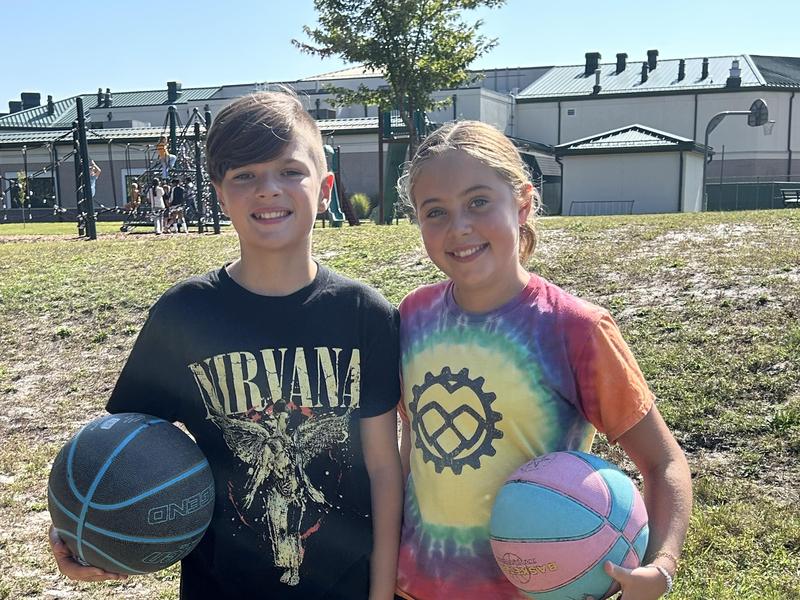 Two children smiling while holding basketballs outdoors.