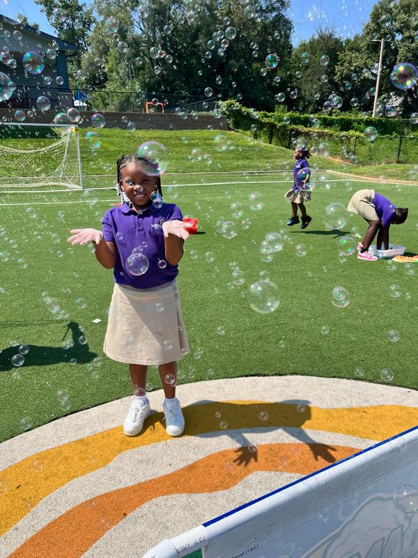 A scholar stands in the middle of bubbles on the soccer field