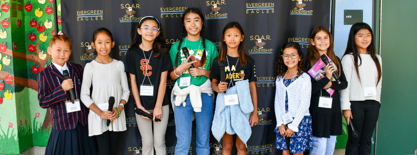 A group of young girls in formal wear posing together at an event backdrop.