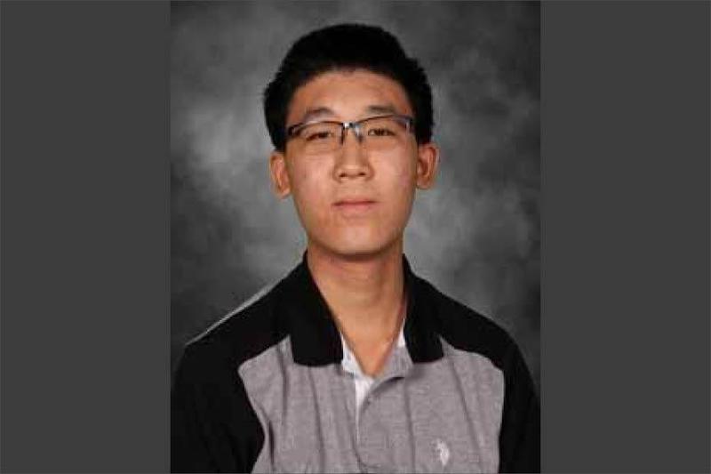 Young man wearing glasses and a collared shirt with a gray background.