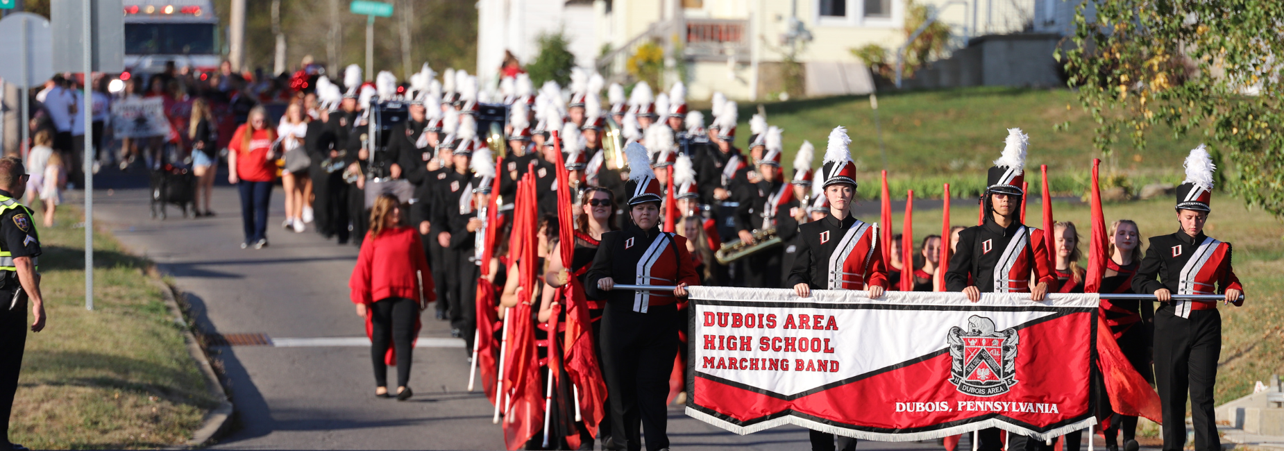 A marching band in uniforms parading down a street with colorful banners and flags.