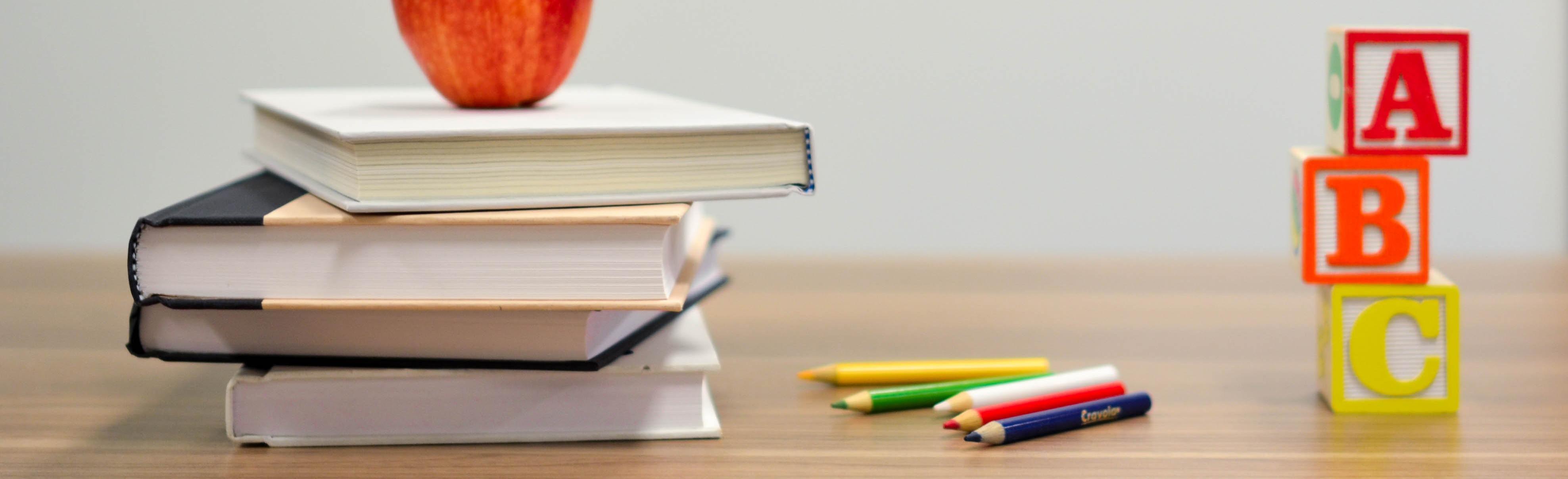 Stack of books with an apple and colored pencils