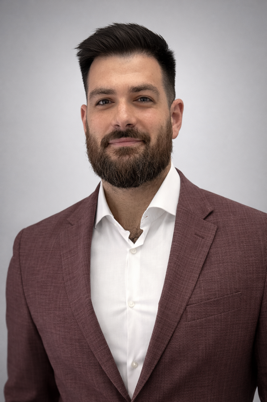 Image of headshot of man with a mustache and beard wearing a brown blazer and white shirt