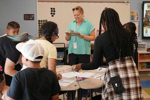 Teacher with clipboard with group standing around table