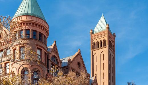 Historic building with intricate architecture and distinctive green domes against a blue sky.