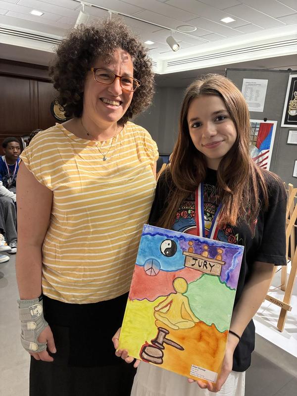 Two women stand together, one holding a colorful artwork depicting peace and balance.