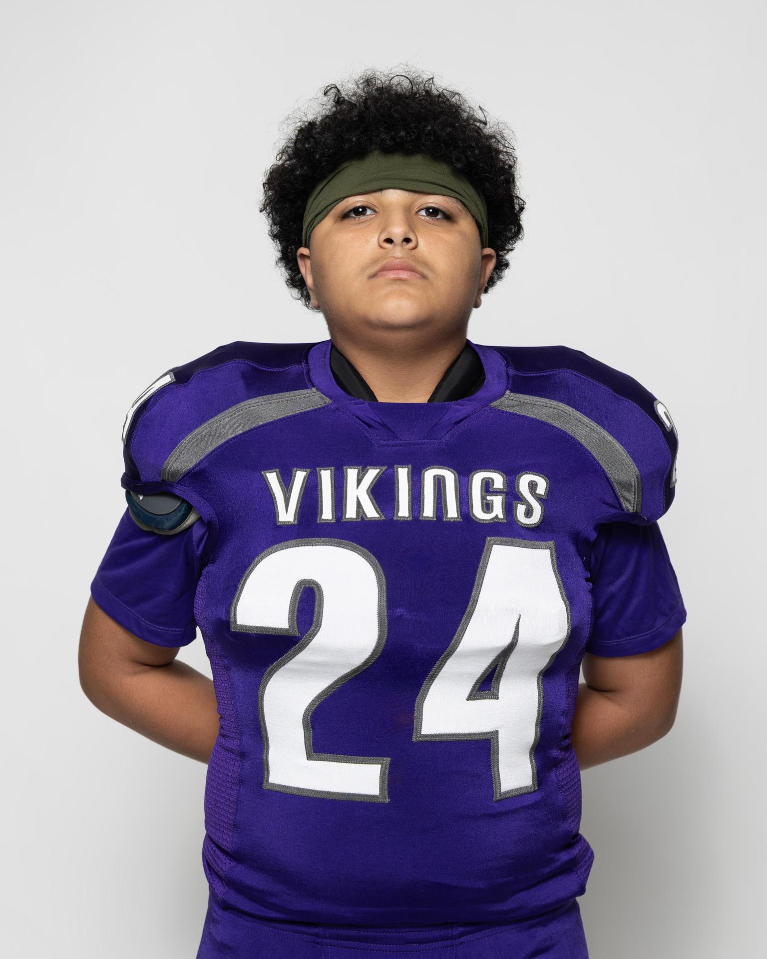Football player with curly hair in a purple Vikings jersey and headband, looking serious.