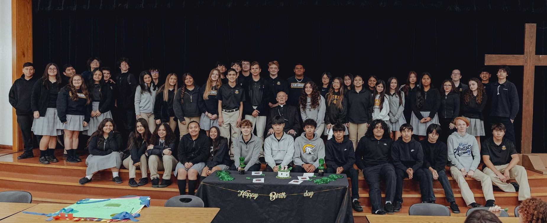 Group of students gathered in a classroom setting for a birthday celebration.