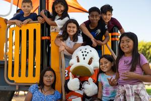 Wild Wing posing with a small group of smiling kids on the playground.