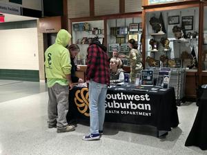 Two individuals converse at a health department table in a school lobby.