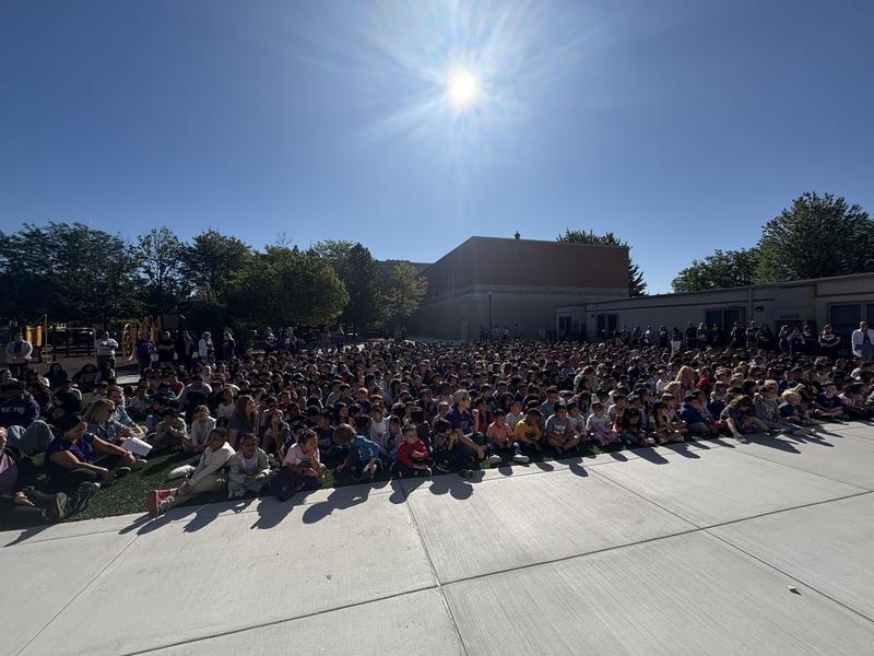 A large crowd of students seated outdoors under a clear blue sky.