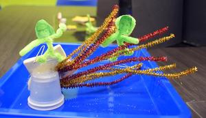 Craft figures on a blue tray with pipe cleaners and a small container.