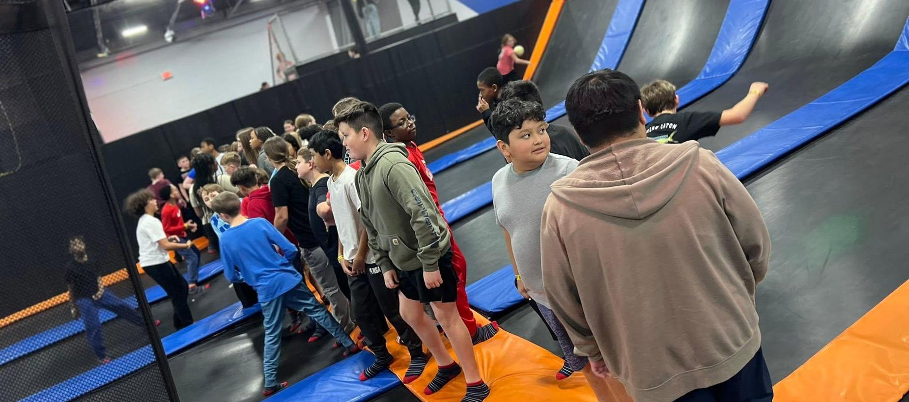 A group of children and teenagers waiting near trampolines in a trampoline park.