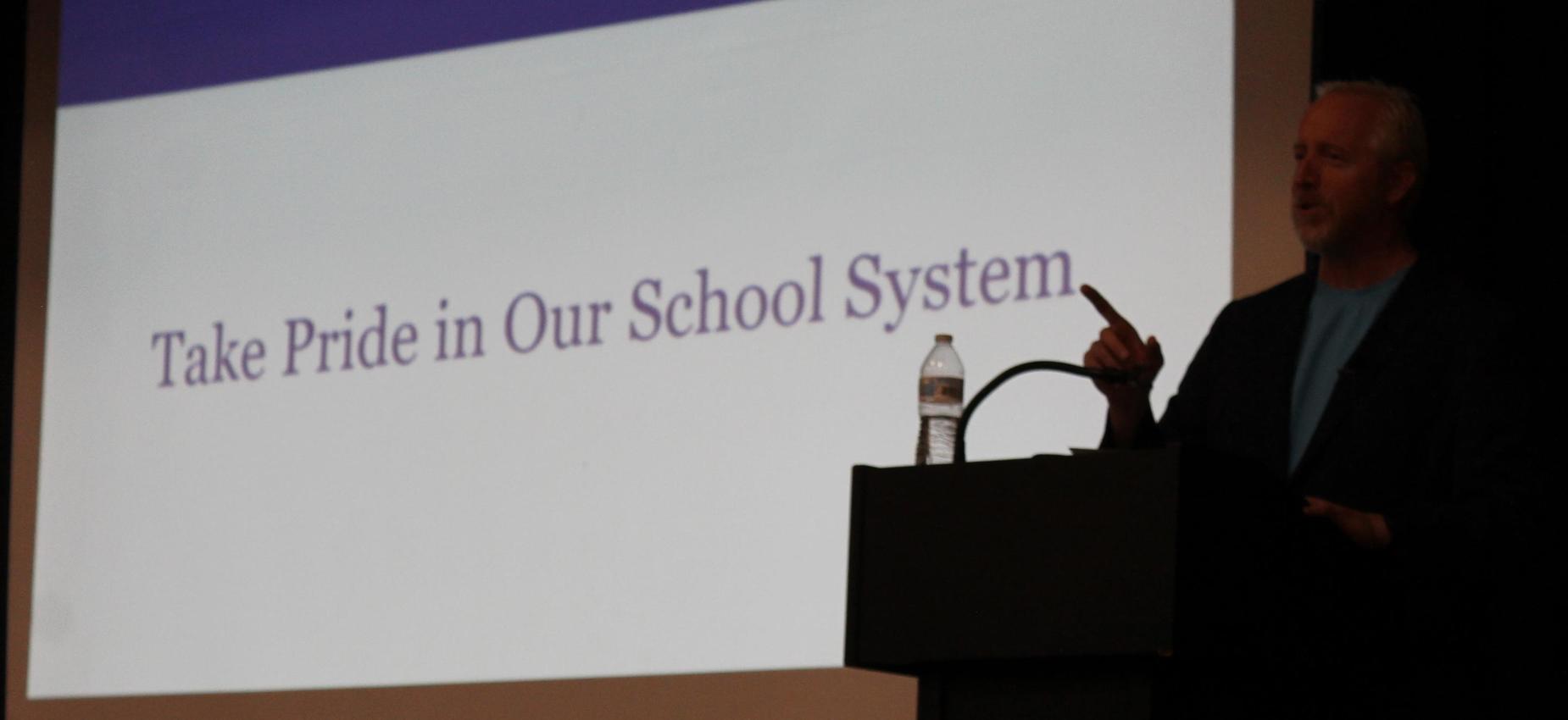 Speaker addressing an audience with a presentation slide behind.