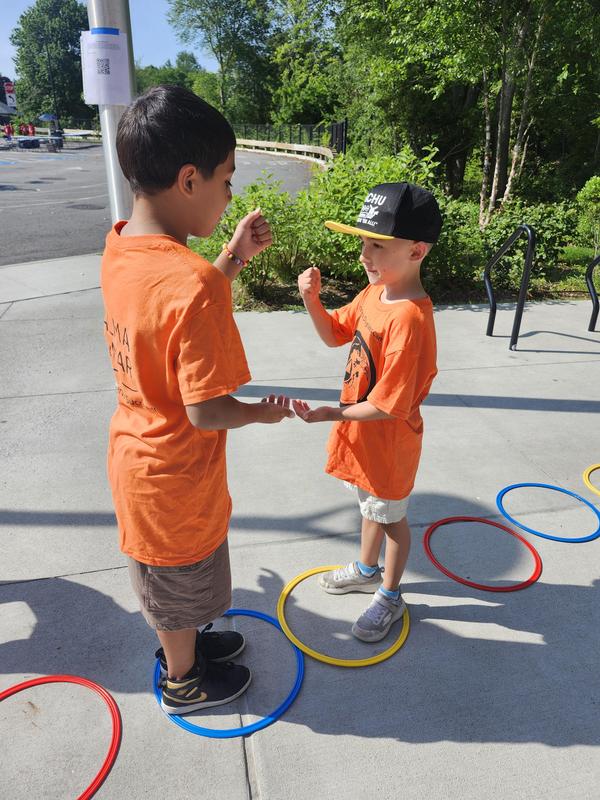 Two scholars play rock, paper, scissor while standing on sidewalk in front of school