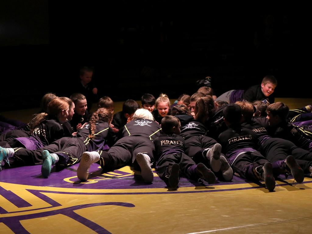 The Girls Wrestling Team on the floor in a circle laying on their stomachs and facing one another in the spotlight.