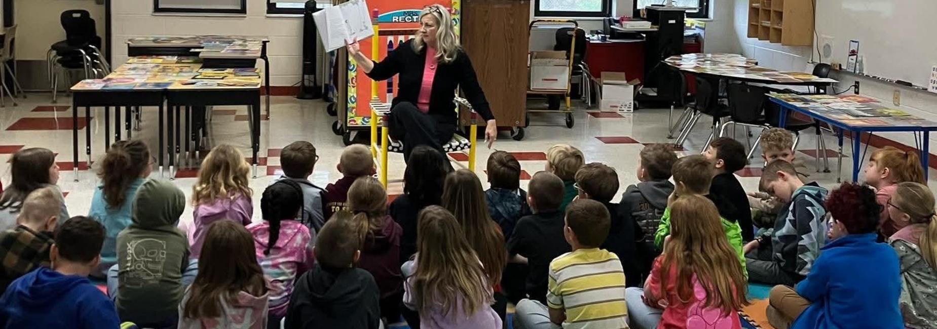 Students sitting lined up in front of a teacher reading