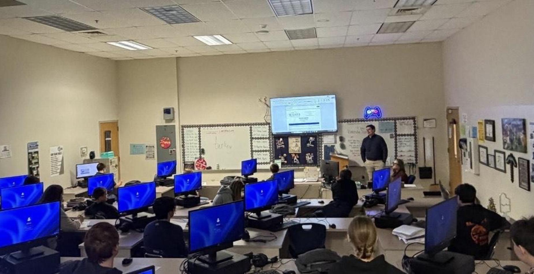 Another classroom with a teacher and students at computers in a similar setup.