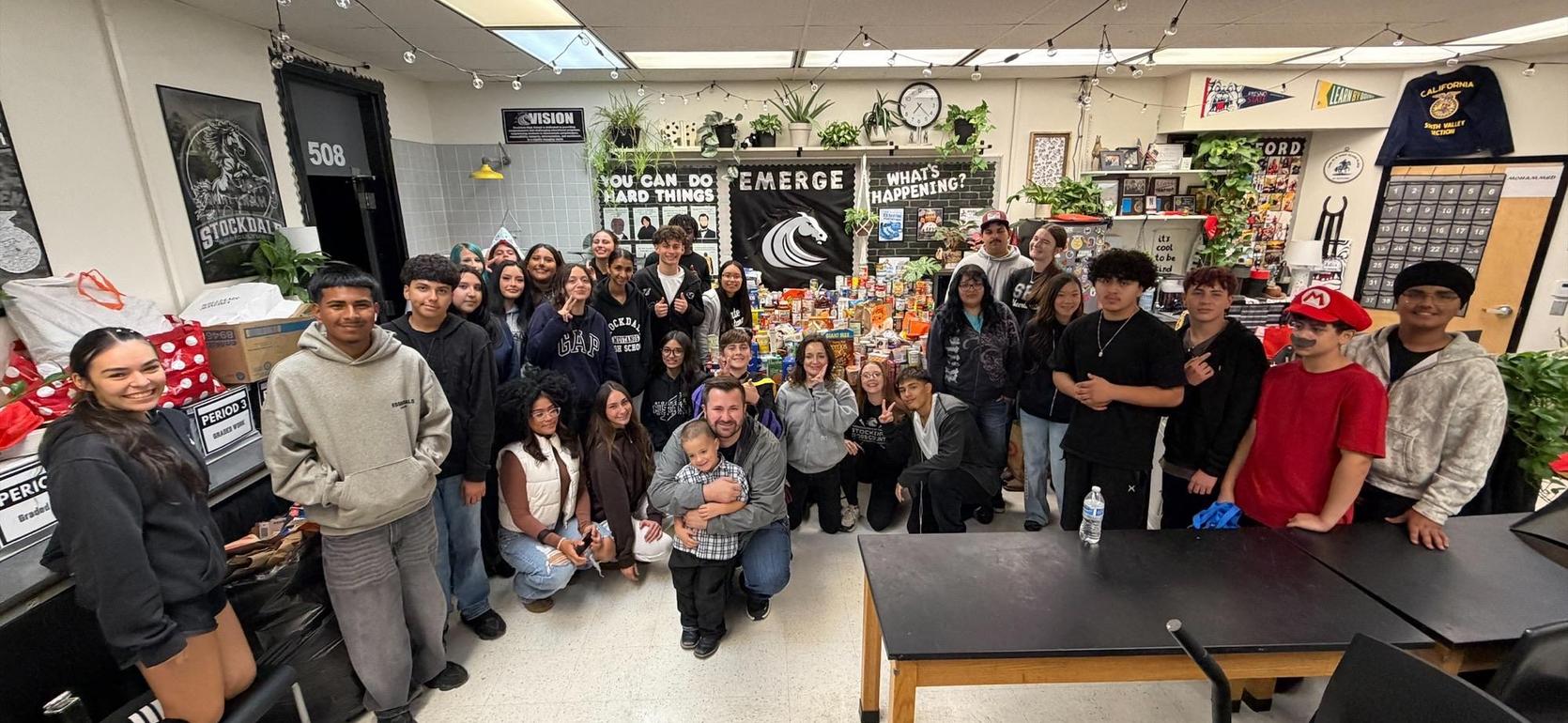 A large group of students and teachers posing together with various decorations in a classroom.