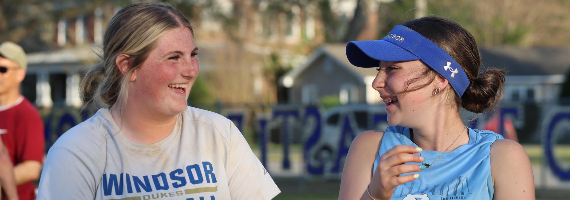 Two young women smiling and chatting during a sports event.