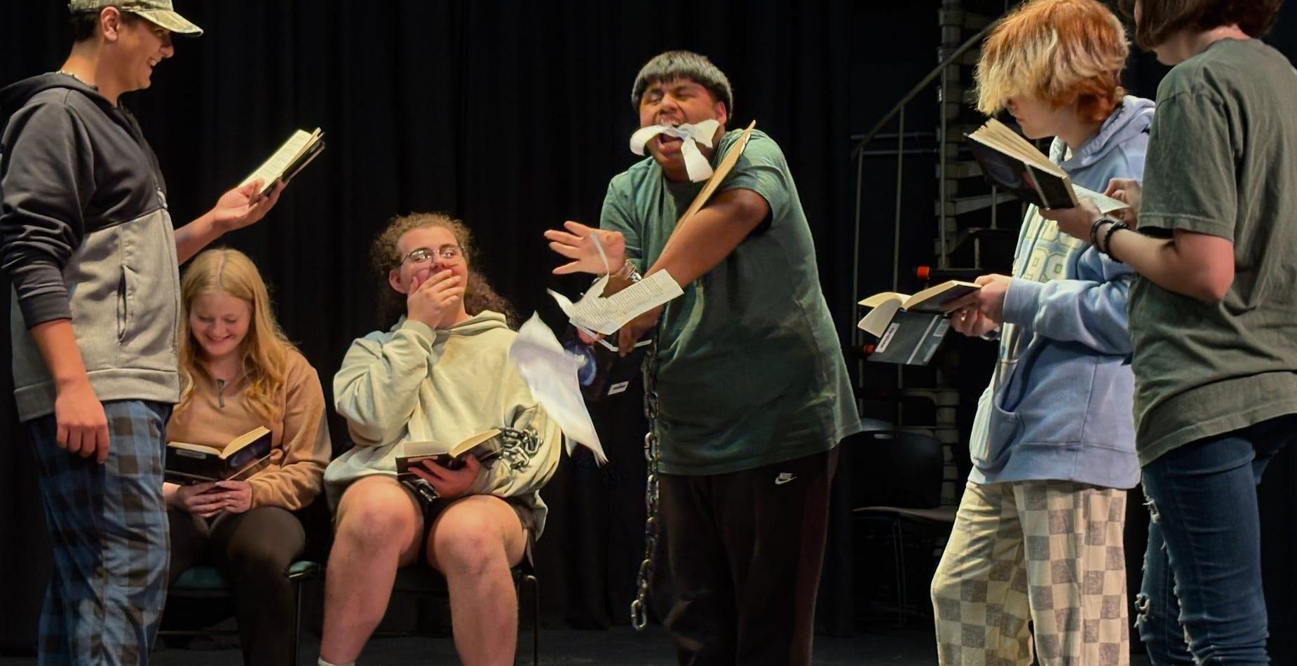 A group of students performing a dramatic reading, holding books and expressing emotions during Ms. Jones class