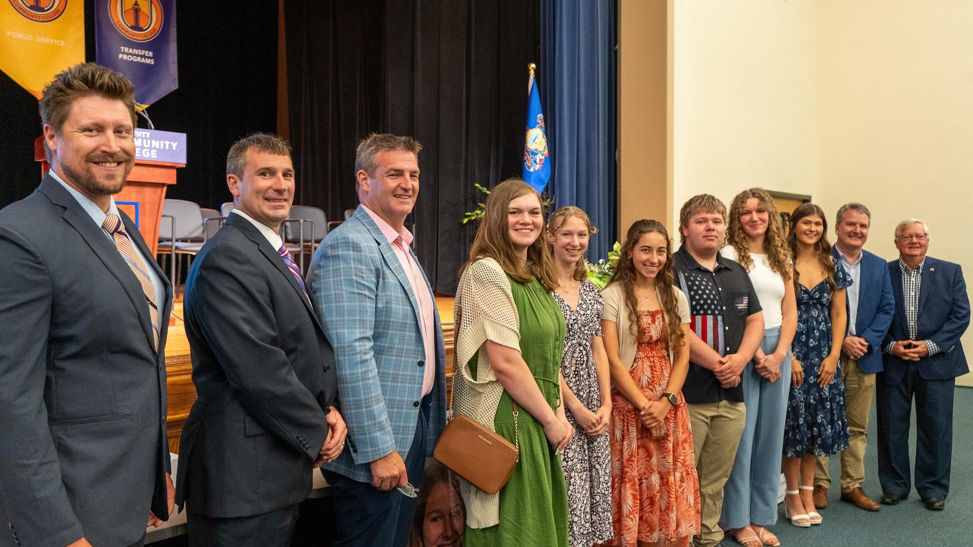 A group photo of students, scholarship sponsors, and Executive Director Brad Whitman poses in front of a stage during a Class Act Scholarship Ceremony.